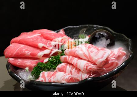 Nahaufnahme von Rind- und Lammfleischbrötchen auf dem Teller. Rohkost für Hot Pot. Unscharfer dunkler Hintergrund Stockfoto