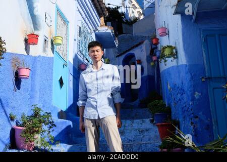 Ein asiatischer junger Mann, der auf einer Treppe in Chefchaouen Marokko steht. Blau gestrichene Häuser herum. Stockfoto