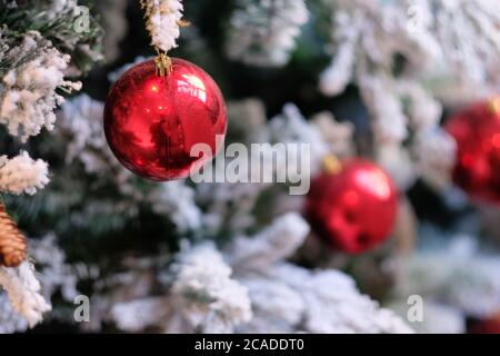 Nahaufnahme glänzende rote Kugel auf weihnachtsbaum. Weichzeichnen weißen Schnee und Ornamente Hintergrund Stockfoto