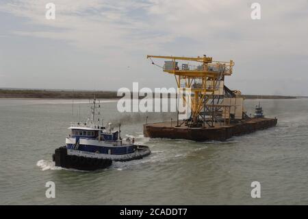 Port Aransas, Texas, USA, 15. Januar 2006: Ein Binnenschiff mit einer Flachwasserbohrplattform und einem Kran wird von einem Schlepper aus der Aransas Bay gezogen. ©Bob Daemmrich Stockfoto