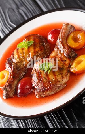 Gegrilltes Schweinekotelett mit reifen Pflaumen und Sauce close-up in einem Teller auf dem Tisch. Vertikal Stockfoto