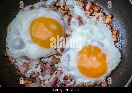 Blick von oben auf zwei Eier mit sonniger Seite oben und Speck in einer Pfanne als Teil des Frühstücks Stockfoto