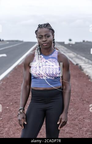 Leistungsstarke afroamerikanische Sportlerin in Sportkleidung, die beim Lauftraining am Straßenrand auf die Kamera schaut Stockfoto