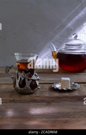 Türkischer Tee in einer traditionellen Tasse mit einer Glas-Teekanne auf einem Holztisch. Teetrinken mit orientalischen Süßigkeiten und einem heißen Getränk. Speicherplatz kopieren. Stockfoto