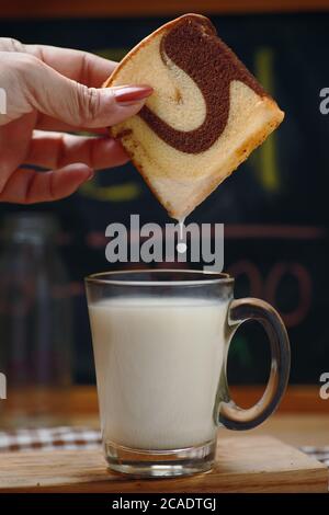 Die Hand der Frau taucht den Marmorkuchen in die Milch In einem Glas Milch Stockfoto