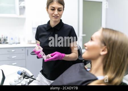 Schönes Lächeln und weiße Zähne einer jungen Frau. Nahaufnahme der Hände des Zahnarztes, die weiblichen Patienten in der Klinik das Zahnmodell erklären Stockfoto