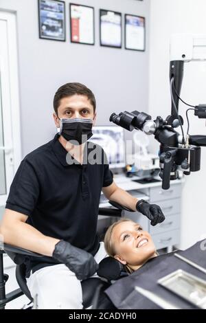 Wir verbessern Ihr Lächeln. Männliche Zahnarzt betrachten den Patienten mit professionellen zahnärztlichen binokularen Mikroskop. Stockfoto