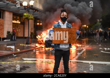 Seattle, USA, 30. Mai 2020: Ein Aktivist hält ein Zeichen NO JUSTICE NO PEACE, während ein Polizeiauto in Westlake im Hintergrund brennt. Stockfoto