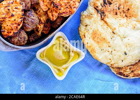 Köstlicher Hummus mit frischem Olivenöl in einer weißen Schüssel, Pitta-Brot, bbq-Fleisch-Kebabs und Steak. Traditionelles Barbecue am Tag der israelischen Unabhängigkeit. Essen auf Blue Vintage Tischdecke serviert. Stockfoto