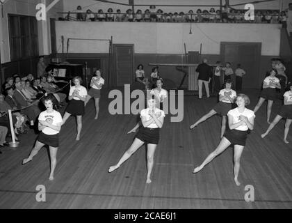 Um 1940er Jahre, historische, weibliche Gymnasiasten in einem Fitnessstudio, die eine künstlerische oder bodengymnastische Ausstellung vor Eltern und Gästen machen, MA, USA. Stockfoto