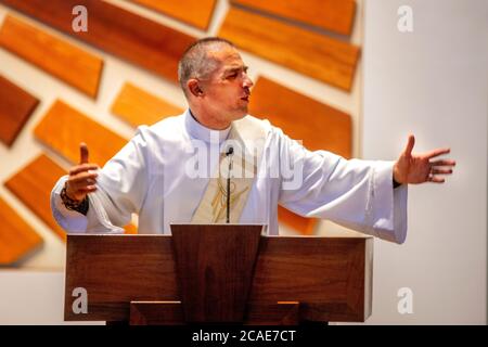 In einem weißen Gewand predigt ein begeisterter Diakon eine Predigt auf der Kanzel einer katholischen Kirche in Tustin, CA. Stockfoto