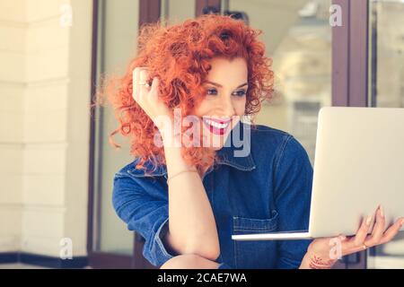 Hübsche Studentin mit niedlichem Lächeln beim Blick auf net-book Laptop während der Entspannung nach Vorlesungen in der Nähe der Universität auf der Treppe, schöne glückliche Frau arbeiten Stockfoto