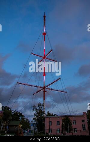 Juschno-Sachalinsk, Russland - 29. August 2019. Rot-weißer Fernsehturm mit schöner Beleuchtung auf der Victory Avenue am Abend. Stockfoto