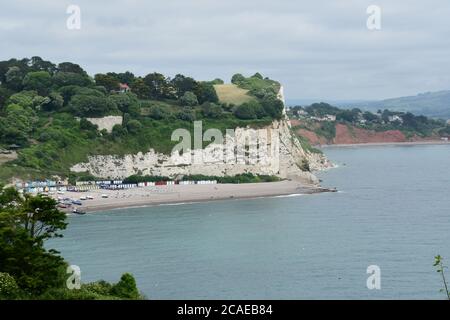 Die bunten Strandhütten am Kiesstrand des Fischerdorfes Beer in Devon, überschattet von der Kreidefelsen, ein Eindringen in den roten Sandsto Stockfoto