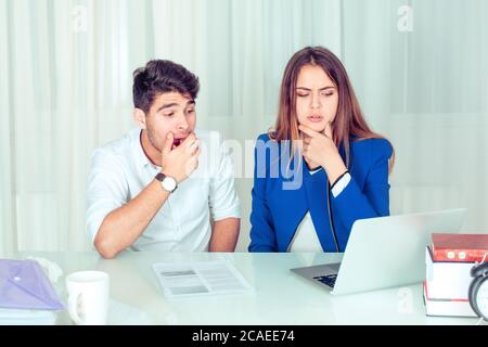 Junge gelangweilte Mann und besorgte Frau Paar Kollegen ungläubig sitzen am Schreibtisch, Laptop mit starken Emotionen am Tisch im Büro Wohnzimmer beobachten Stockfoto