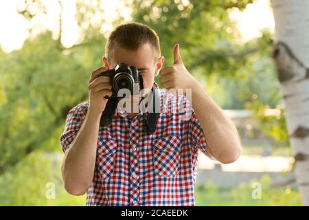 Der Fotograf fotografiert vor dem Hintergrund von Grün. Vorderansicht. Daumen hoch Stockfoto