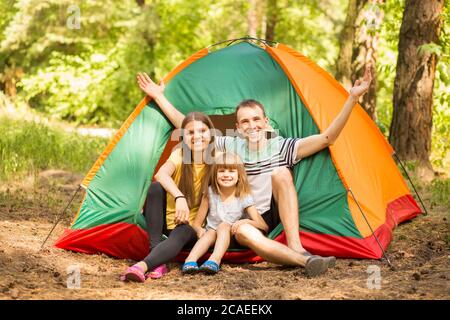 Outdoor-Porträt von jungen glücklichen Familie genießen Natur sitzen in der Nähe von Camp Zelt im Sommerwald Stockfoto