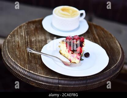 Köstliches Dessert auf braunem strukturiertem Hintergrund. Patisserie-Konzept. Ein Stück Kuchen mit Brombeeren und Himbeeren in der Nähe von Heißgetränk. Käsekuchen mit Beeren und Kaffee auf Holztisch, Nahaufnahme Stockfoto