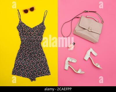 Blumenoveralls, rosa Handtasche, weiße Schuhe und rosafarbene Brille. Heller rosa und gelber Hintergrund, Nahaufnahme Stockfoto