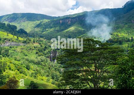 Erstaunliche Landschaft von Sri Lanka. Wasserfall in den Bergen und Teeplantage. Rauch hinter Bäumen. Stockfoto