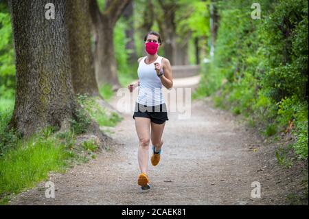 Bleiben Sie während des Coronavirus fit. Eine sportliche Frau joggt draußen, sie hat eine Schutzmaske im Gesicht. Laufen in den Tagen des Covid-19. Stockfoto