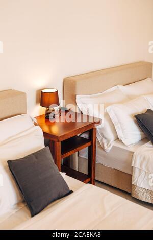 Zwei Betten mit weißen und schwarzen Kissen und ein Holztisch mit einer Nachtlampe dazwischen. Stockfoto