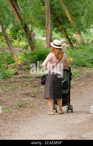 Frau mit Kinderwagen beim Spaziergang durch den grünen Wald Stockfoto