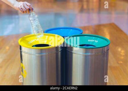 Frau, die leere Plastikflaschen in den Papierkorb im Einkaufszentrum stellt. Verschiedene Mülleimer mit bunten Mülltüten. Stockfoto