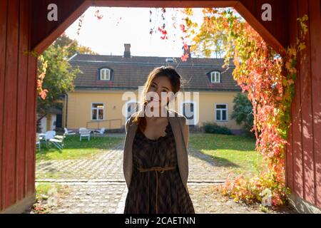 Junge glückliche asiatische Frau lächelt im hölzernen Eingang des eleganten Vorstadthauses Stockfoto