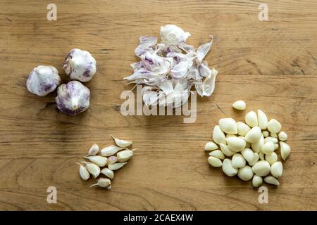 Eine Übersicht über Knoblauchzwiebeln, Nelken und Schalen auf einem hölzernen Schneidebrett. Stockfoto