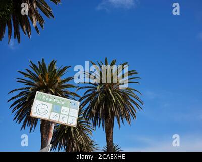 Low-Angle-Ansicht eines Schildes am Sea Point, Kapstadt mit einem Smiley-Gesicht. Palmen, blauer Himmel und Wolken im Blick. Stockfoto
