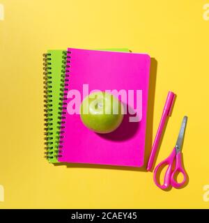 Schule helle Vorräte, Notizbücher, Schere, Apfel auf gelbem Hintergrund. Draufsicht, flach liegend. Stockfoto