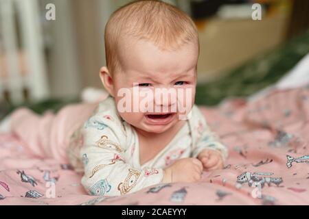 Drei Monate altes Mädchen weinend, liegt auf dem Bauch und ist sehr aufgeregt, traurige Emotionen im Kind Stockfoto