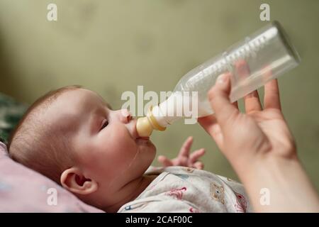 Neugeborenes Baby isst Milch aus der Flasche, Tropfen der Nahrung heruntergelaufen Wange, Papa gibt Baby-Mischung Stockfoto