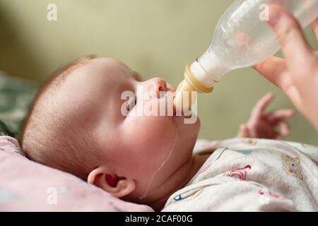 Neugeborenes Baby isst Milch aus der Flasche, Tropfen der Nahrung heruntergelaufen Wange, Papa gibt Baby-Mischung Stockfoto