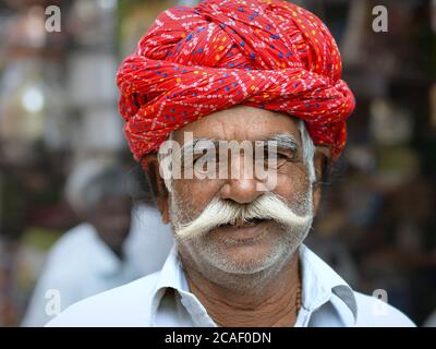 Freundliche ältere indische Rajasthani Mann mit roten Turban und weißen Schnurrbart Posen für die Kamera. Stockfoto