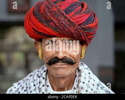 Indian Rajasthani Mann mit schwarzem Schnurrbart, rot-und-schwarz Turban und Gold Ohrringe Posen für die Kamera. Stockfoto