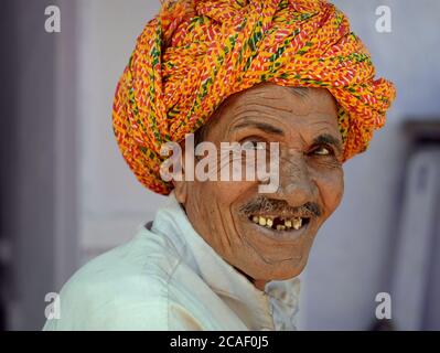 Alter, lächelnder indischer Rajasthani Mann mit schlechten Zähnen trägt einen bunten Rajasthani Turban (Pagari) und schaut auf die Kamera. Stockfoto