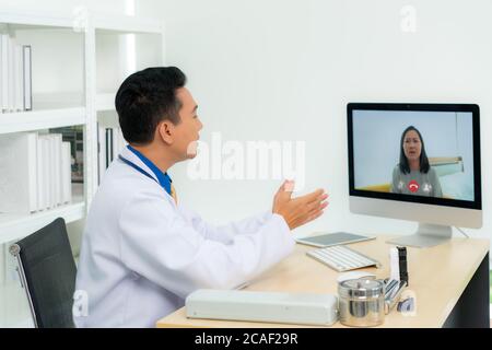 Asiatischer Mann Arzt trägt weißen Mantel und Headset sprechen Videokonferenzen auf Laptop-Computer mit Online-Videoanruf Beratung App. Medizinische Fernversorgung Stockfoto