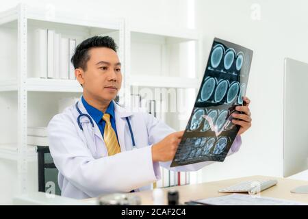 Asiatischer Mann Arzt hält und schaut zu untersuchen Röntgenbild des Patienten Schädel und Gehirn in einer medizinischen Klinik im Krankenhaus. Stockfoto