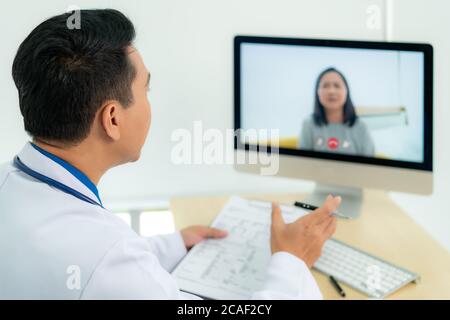 Asiatischer Mann Arzt trägt weißen Mantel und Headset sprechen Videokonferenzen auf Laptop-Computer mit Online-Videoanruf Beratung App. Medizinische Fernversorgung Stockfoto