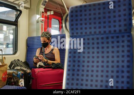 Kaukasische weibliche Reisende mit Gesichtsschutz Maske sitzen und verwenden Handy in DB Zug in Deutschland während der Epidemie der COVID-19 Virus mit neuem Normal Stockfoto