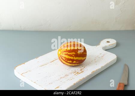 Kleine vietnamesische Melone auf einem Schneidebrett auf grauem Hintergrund. Miniaturfrucht mit Ananasgeschmack. Speicherplatz kopieren. Horizontale Ausrichtung. Stockfoto