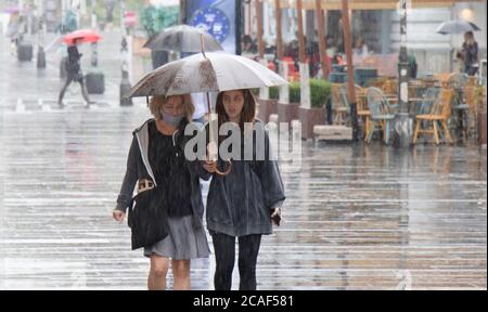 Belgrad, Serbien - 5. August 2020: Menschen unter Sonnenschirmen gehen an einem regnerischen Sommertag in der Stadt auf der Fußgängerzone Stockfoto