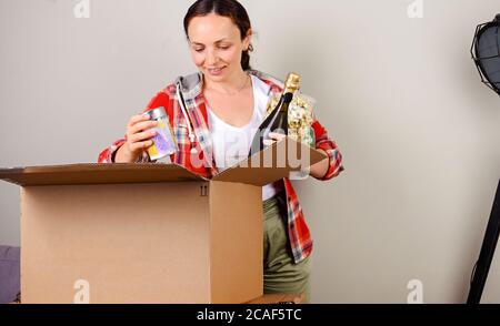 Paket auspacken. Die Frau öffnet die Box und nimmt die Einkäufe gerne aus dem Online-Shop. Liefer- und Servicekonzept. Online-Shopping. Die Person ist Europäer. Freier Speicherplatz für Text Stockfoto