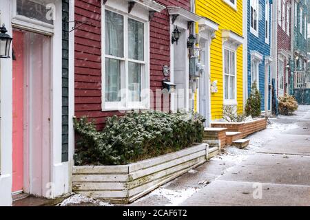 Außenansicht von mehreren bunten angrenzenden Reihenhäusern mit großen Fenstern und Türen. Es gibt Schnee auf dem Boden und Bürgersteig in der Nähe der Gebäude. Stockfoto