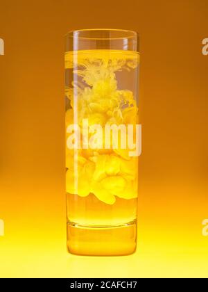 Tintenwolke in sauberem Glas. Gelbe Farbe in Wasser. Monochromes Schema. Konzept der kreativen Cocktails. Stockfoto
