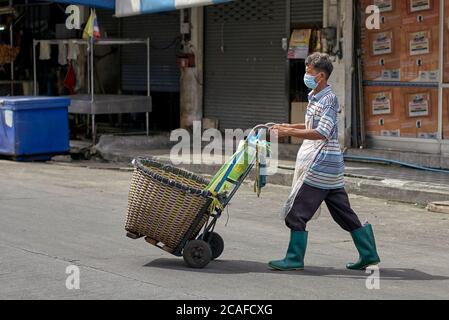 Thailand Straßenszene mit Mann trägt eine Covid-19 Gesichtsmaske und mit einem Handwagen, um Marktware zu sammeln. Thailand S. E. Asien Stockfoto