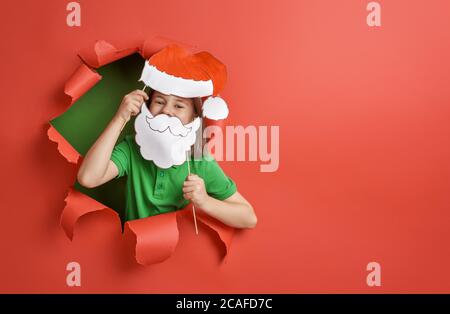 Frohe Weihnachten! Kleines Mädchen in Santa Hut auf hellen Farben Hintergrund. Rot und grün. Stockfoto