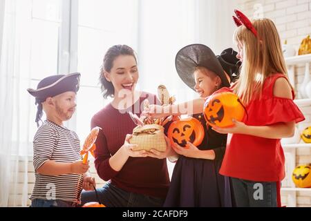 Glückliche Familie feiert Halloween! Junge Mutter behandelt Kinder mit Süßigkeiten. Lustige Kinder in Faschingskostümen. Stockfoto